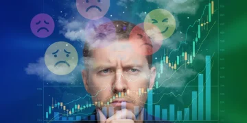 Pessoa pensativa diante de gráficos financeiros, simbolizando a psicologia do dinheiro e decisões financeiras.